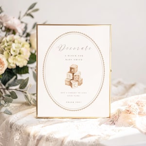 May include: A framed sign with gold trim and the text "Decorate" in elegant script. The sign includes the text "A block for Baby Smith" and a stack of toy blocks. The bottom of the sign reads "Don't forget to sign your name. Thank you!"