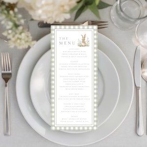 Puede incluir: Una mesa formal con platos blancos, cubiertos y un menú. El menú presenta una ilustración de un conejito y un borde a cuadros verdes y blancos. El menú enumera aperitivos, entrantes, platos principales, postres y bebidas.