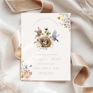 Pode incluir: Um cartão de convite creme com ilustrações florais e de pássaros. O cartão apresenta um ninho com ovos, rodeado por pássaros e flores. O texto inclui "Let's Feather the Nest Together" e detalhes do evento.