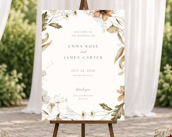 May include: A rectangular wedding welcome sign on a wooden easel featuring a white background with watercolor botanical illustrations of brown and green leaves and flowers. The text reads: Welcome to the wedding of Emma Rose and James Carter, Oct 24, 2026, The Willow Estate, thank you for celebrating with us.