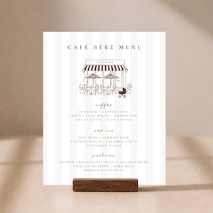 May include: A vertical menu card titled CAFÉ BÉBÉ MENU with a white and light grey striped background. It features a brown line drawing of a cafe storefront with tables, chairs, and a baby carriage. The text lists coffee, add-ons, and pastries.