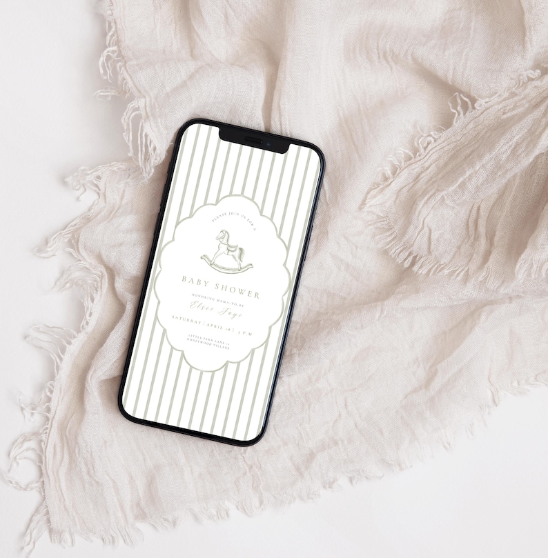 May include: A smartphone screen shows a baby shower invitation with a rocking horse design. The invitation has vertical stripes and a decorative border. The text reads "Baby Shower" and includes event details. The phone is on cream-coloured fabric.