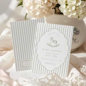 May include: Two baby shower invitations with a pale green stripe pattern. One invitation features a rocking horse graphic and text that reads "Baby Shower" and "Elsie Foye". The invitations are on a white surface with a vase of white flowers in the background.