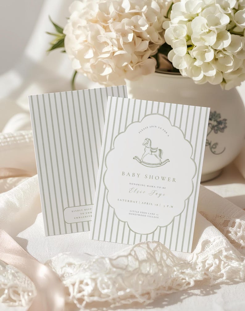 May include: Two baby shower invitations with a pale green stripe pattern. One invitation features a rocking horse graphic and text that reads "Baby Shower" and "Elsie Foye". The invitations are on a white surface with a vase of white flowers in the background.