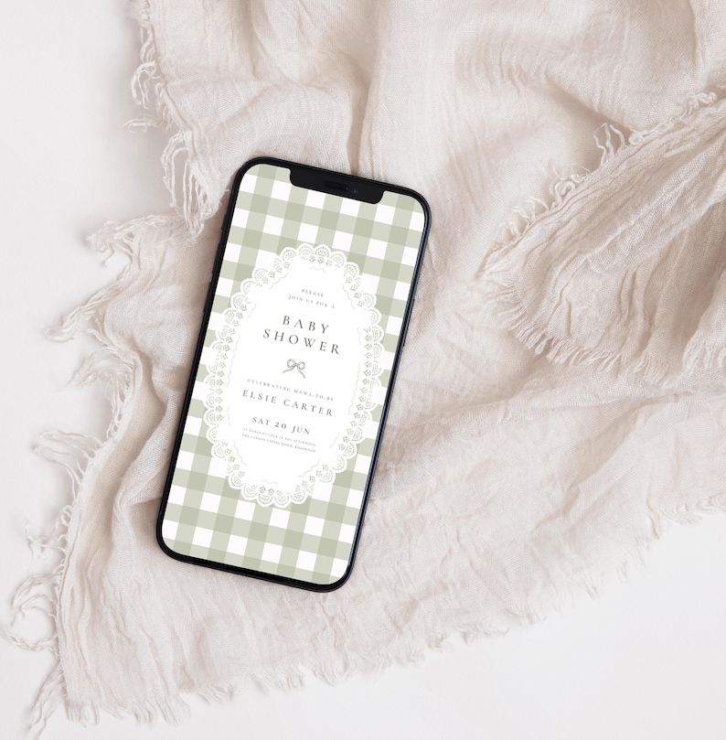 Puede incluir: Un tel&eacute;fono inteligente muestra una invitaci&oacute;n a un baby shower. La pantalla presenta un patr&oacute;n de cuadros vichy verde salvia y blanco con un marco ovalado blanco similar al encaje. El texto de la invitaci&oacute;n dice "Baby Shower" y "Elsie Carter".