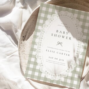 Puede incluir: Una invitaci&oacute;n a un baby shower con un fondo de patr&oacute;n de cuadros vichy verde salvia. La invitaci&oacute;n presenta un dise&ntilde;o de encaje ovalado blanco con las palabras "Baby Shower" y detalles del evento de Elsie Carter. La invitaci&oacute;n est&aacute; sobre un plato de tonos neutros.
