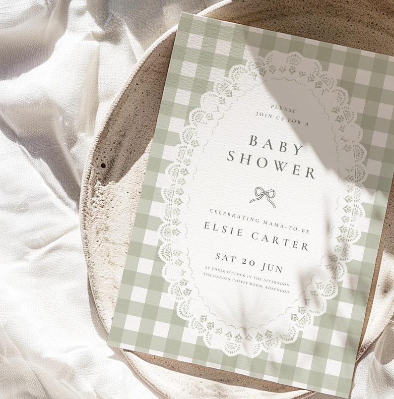 Puede incluir: Una invitaci&oacute;n a un baby shower con un fondo de patr&oacute;n de cuadros vichy verde salvia. La invitaci&oacute;n presenta un dise&ntilde;o de encaje ovalado blanco con las palabras "Baby Shower" y detalles del evento de Elsie Carter. La invitaci&oacute;n est&aacute; sobre un plato de tonos neutros.
