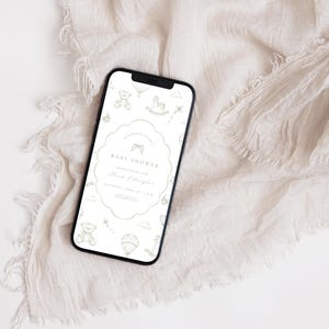 May include: A smartphone screen shows a baby shower invitation. The invitation has a scalloped edge and includes text with the words "Baby Shower" and event details. The background is a soft, neutral colour with baby-themed illustrations.