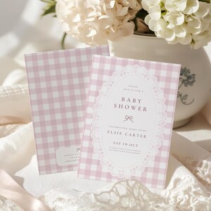 May include: Two rectangular baby shower invitation cards featuring a light pink and white gingham pattern. The front card displays a white oval frame with lace-like edges, containing the text: Please join us for a Baby Shower, Elsie Carter, Sat 10 Oct.
