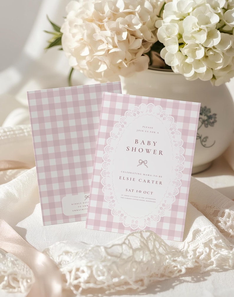 May include: Two rectangular baby shower invitation cards featuring a light pink and white gingham pattern. The front card displays a white oval frame with lace-like edges, containing the text: Please join us for a Baby Shower, Elsie Carter, Sat 10 Oct.
