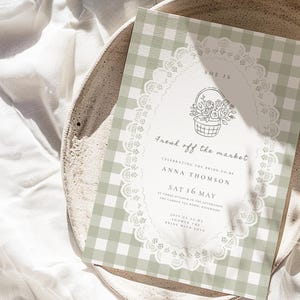 May include: A wedding invitation with a green and white gingham pattern background. The invitation features a floral basket illustration and the text "Fresh off the market". The invitation is on a white plate.