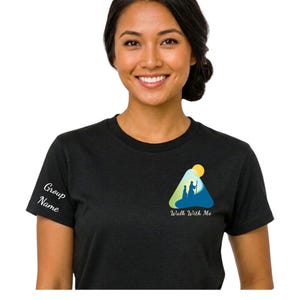 Puede incluir: Camiseta negra con un gráfico en la parte delantera que presenta una escena de montaña con dos figuras y el texto "Walk With Me". La manga tiene el texto "Group Name".
