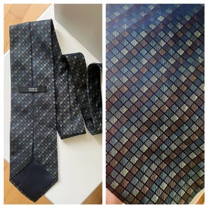 May include: A dark blue tie with a repeating diamond pattern in shades of blue, brown, and grey. The tie has a label that reads "MARKS & SPENCER". The tie is displayed on a white surface.