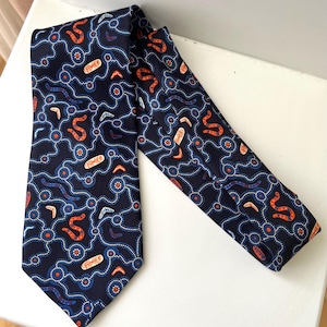 May include: A dark navy blue necktie featuring a repeating pattern of orange and white dotted lines, small orange and white boomerang shapes, and stylized orange and white oblong symbols arranged across the entire surface of the fabric.