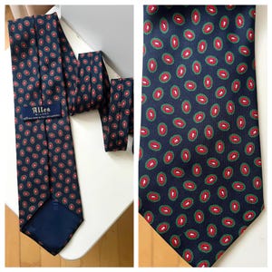 May include: Navy blue silk tie with a repeating pattern of red and green ovals. The tie has a label that reads "Altea Milano". The tie is made of silk and has a classic design.