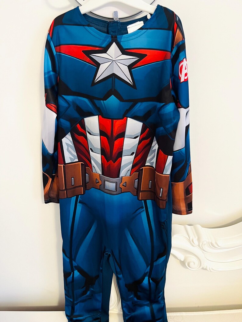 May include: A blue Captain America costume with a white star on the chest. The costume features a red and white design on the chest and a brown belt. The long-sleeved jumpsuit has the Avengers logo on the sleeve.
