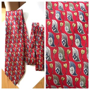 May include: A red necktie with a repeating pattern of paisley shapes and floral elements in shades of blue, green, gray, and yellow. The tie is made of a smooth, likely silk, material.