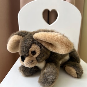 Könnte beinhalten: Ein Plüsch-Hase mit weichem, strukturiertem Fell in Dunkelbraun und Creme. Das Stofftier hat lange, herabhängende Ohren, dunkelbraune Augen, eine kleine schwarze Nase und feine schwarze Schnurrhaare an der Schnauze.
