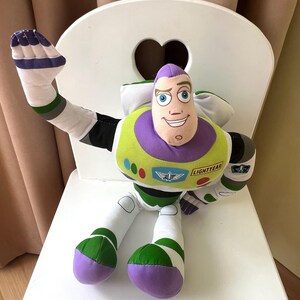 May include: A plush Buzz Lightyear toy, featuring a purple and white head, green and white body, and white arms and legs. The toy is sitting on a white chair with a heart-shaped cutout in the back.