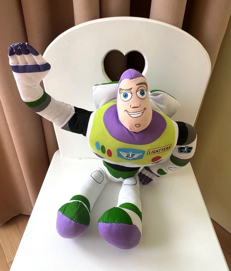 May include: A plush Buzz Lightyear toy, featuring a purple and white head, green and white body, and white arms and legs. The toy is sitting on a white chair with a heart-shaped cutout in the back.