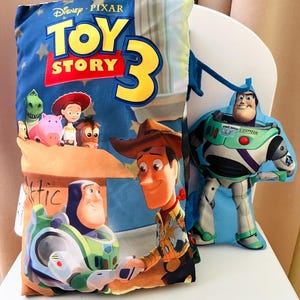 May include: A rectangular pillow featuring the Disney Pixar Toy Story 3 logo, with printed images of Buzz Lightyear, Woody, Jessie, Rex, Hamm, and Bullseye. Beside it is a smaller, die-cut plush pillow shaped like the character Buzz Lightyear.