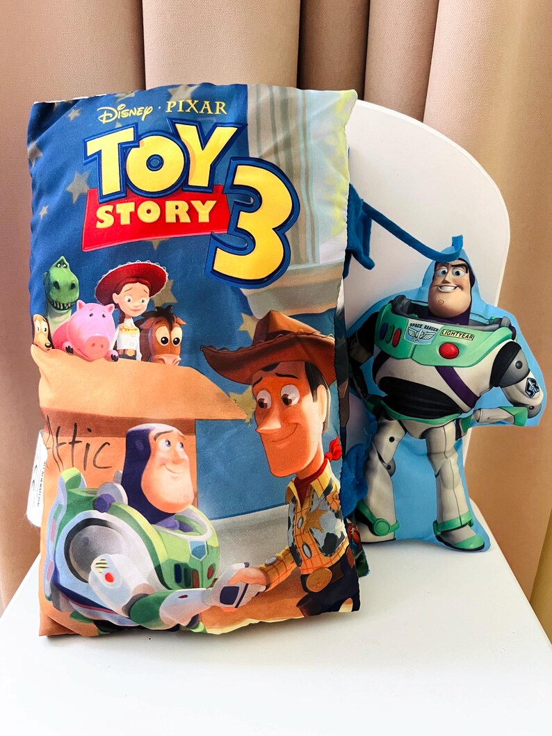 May include: A rectangular pillow featuring the Disney Pixar Toy Story 3 logo, with printed images of Buzz Lightyear, Woody, Jessie, Rex, Hamm, and Bullseye. Beside it is a smaller, die-cut plush pillow shaped like the character Buzz Lightyear.