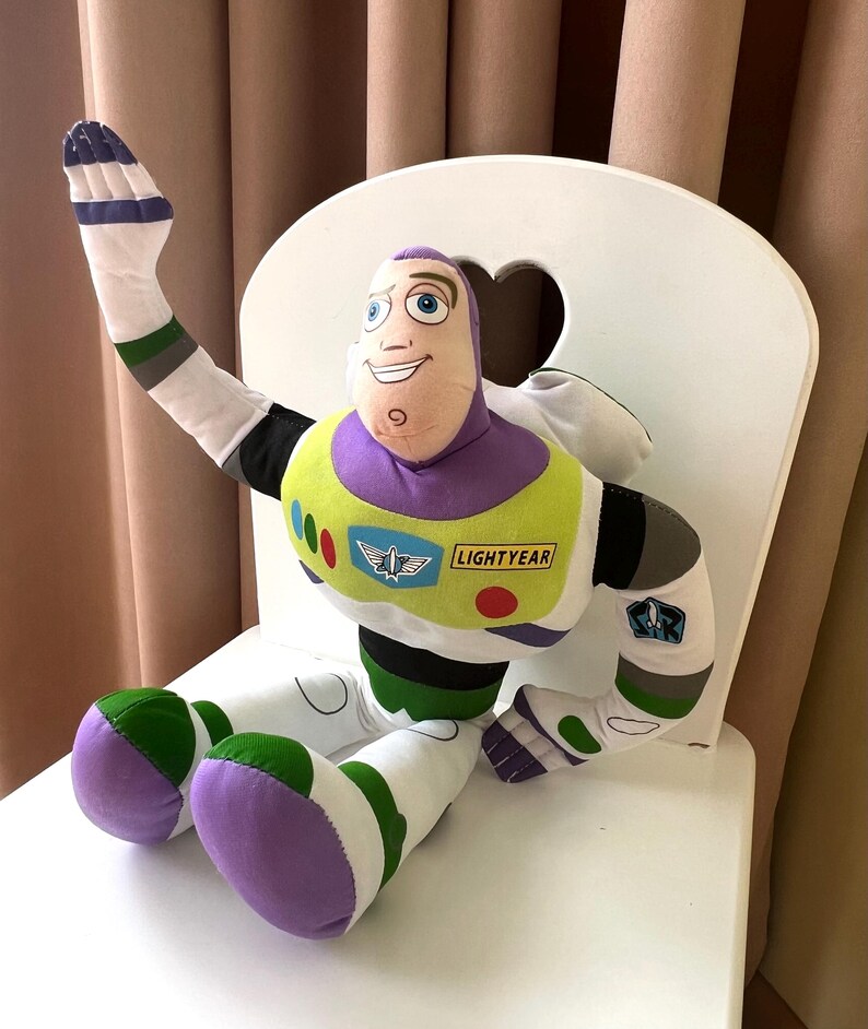 May include: A plush Buzz Lightyear doll, featuring a purple and white space suit with green and yellow accents. The doll has a smiling face and is seated on a white chair. The word "LIGHTYEAR" is visible on the chest.