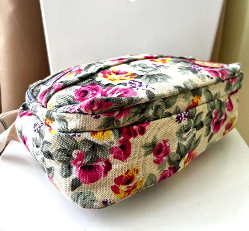 Op de afbeelding: Rechthoekige tas met bloemenprint op een cr&egrave;mekleurige achtergrond. Het patroon bevat roze, gele en rode rozen met groene bladeren. De tas heeft een beige riem en een ritssluiting.