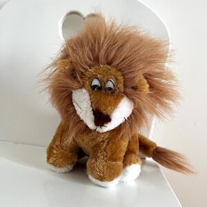 May include: A plush lion toy with a brown body, a fluffy brown mane, and a white muzzle. The lion has a small tail and white paws. It is sitting on a white surface.