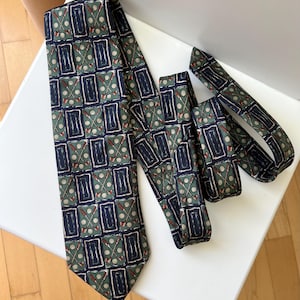 May include: A patterned tie featuring a golf theme. The tie has a dark green background with a repeating pattern of golf clubs, golf balls, and rectangular shapes in navy blue and red. The tie is lying on a white surface.