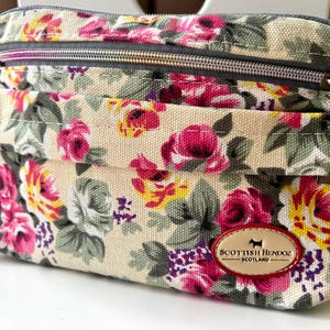 Op de afbeelding: Crossbody tas met een bloemenpatroon met roze, gele en witte rozen op een beige achtergrond. De tas heeft een grijze rits en een klein voorvak. Een leren patch met de tekst "Scottish Henndz Scotland" staat op de voorkant.