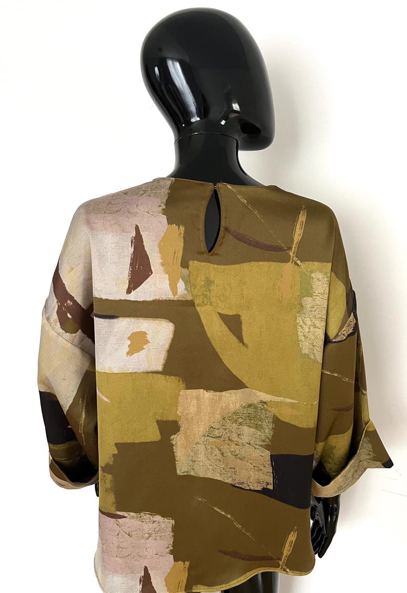May include: A long-sleeved blouse with a unique abstract pattern. The blouse features a keyhole detail at the back and is adorned with a mix of olive green, beige, brown, and white geometric shapes. The sleeves are cuffed at the wrists.
