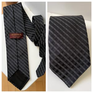 May include: A black silk tie with a subtle grid pattern and a label that reads "Gessner Switzerland Pure Silk." The tie is displayed on a white surface, showcasing its design and texture.