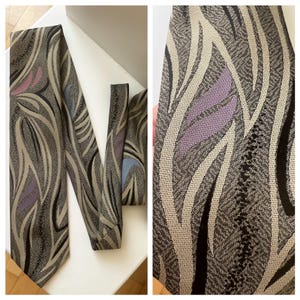 Könnte beinhalten: Gemusterte Krawatte mit abstraktem Design in Grau-, Schwarz-, Beige-, Lavendel- und Blautönen. Die Krawatte hat ein strukturiertes Aussehen und ein klassisches, spitzes Ende. Geeignet für formelle Anlässe.