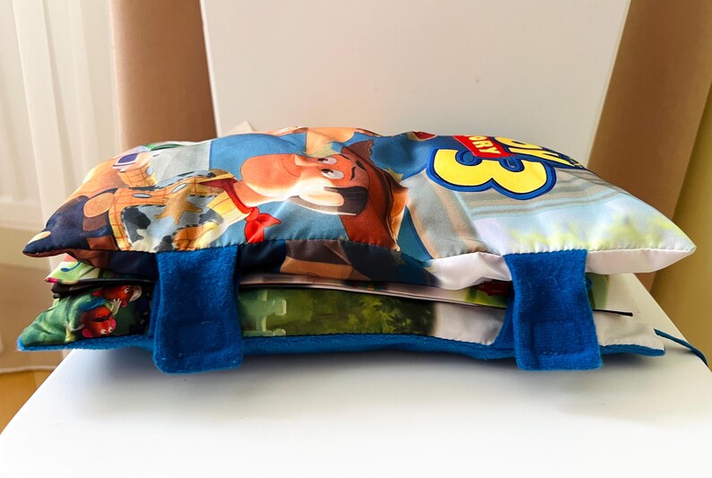 May include: A rectangular Toy Story 3 themed fabric pouch featuring a colorful graphic of Woody on the front. The pouch is secured with two blue felt straps with hook-and-loop fasteners. The design includes the Toy Story 3 logo in yellow and red.