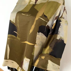 May include: An olive green, beige, and black abstract print blouse with long sleeves. The top has a round neckline and a loose fit. The sleeves have a cuff at the wrist. The fabric has a silky appearance.