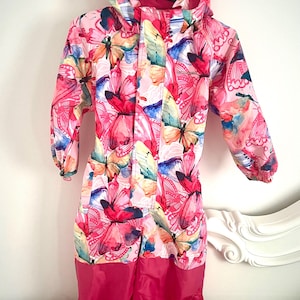 May include: Pink and white children's snowsuit with a colorful butterfly pattern. The snowsuit features a hood, long sleeves, and solid pink legs. The snowsuit is designed for cold weather and outdoor activities.