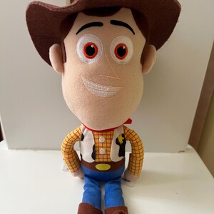 Puede incluir: Un peluche de un personaje de la pel&iacute;cula animada Toy Story. La mu&ntilde;eca tiene un sombrero de vaquero marr&oacute;n, una cara beige con rasgos bordados y un pa&ntilde;uelo rojo. Viste una camisa a cuadros amarilla, un chaleco blanco, vaqueros azules y botas marrones.