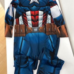 May include: A blue Captain America costume with a white star on the chest. The costume features a red, white, and blue design, with brown belt details. The long-sleeved jumpsuit is made of a shiny material.