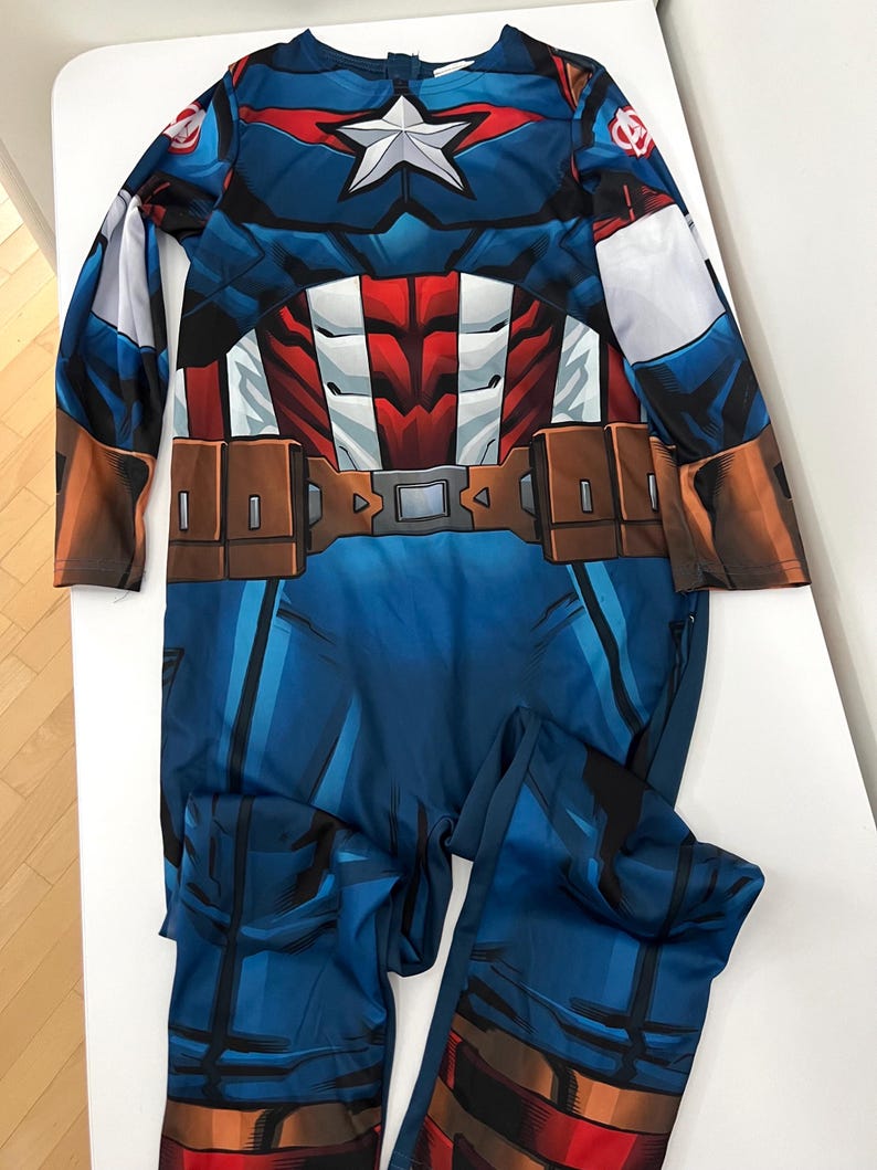 May include: A blue Captain America costume with a white star on the chest. The costume features a red, white, and blue design, with brown belt details. The long-sleeved jumpsuit is made of a shiny material.