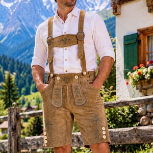 May include: A white long-sleeved button-down shirt paired with tan suede lederhosen featuring suspenders, intricate green floral embroidery, and light-colored buttons on the sides and waistband, worn in a mountainous outdoor setting.