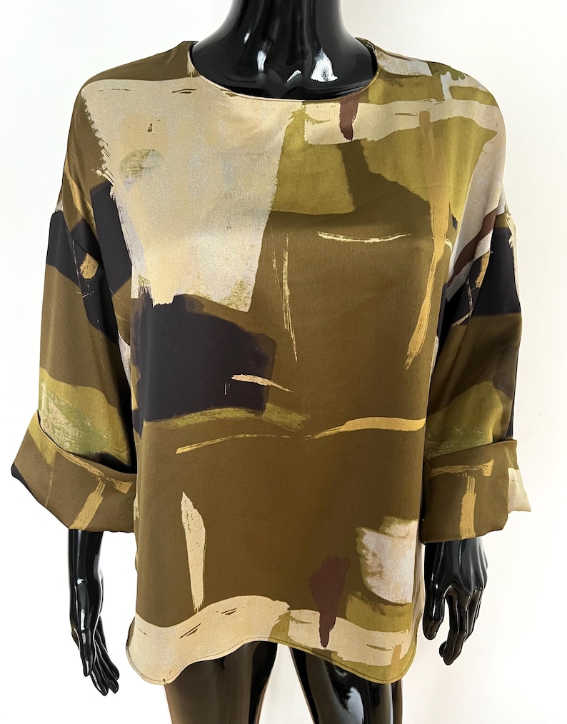 May include: A long-sleeved blouse with a round neckline and rolled-up cuffs. The top features an abstract pattern in shades of olive green, black, beige, and brown. The fabric appears to be a lightweight material, suitable for warmer weather.