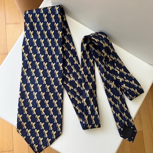 May include: A navy blue tie featuring a repeating pattern of gold-coloured bee illustrations. The tie is displayed on a white surface, highlighting its design and texture. A classic accessory.