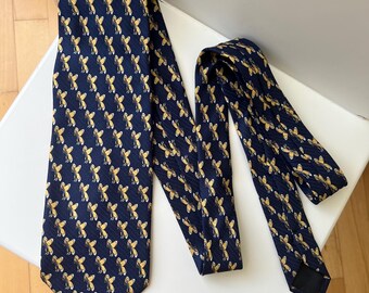 May include: A navy blue tie with a repeating pattern of gold-colored bee illustrations. The tie is displayed on a white surface, showcasing its design and texture. The tie is a classic accessory.