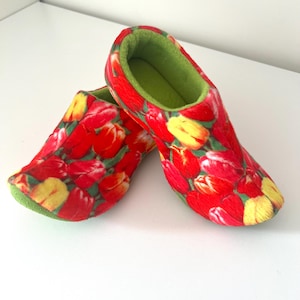 Peut inclure: Une paire de chaussons rouges avec un motif de tulipes aux couleurs vives, jaunes et rouges. L'intérieur est vert vif, offrant un contraste. Ces chaussons sont conçus pour un usage intérieur.