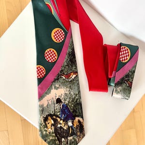 以下が含まれることがあります： 狩猟シーンが描かれたヴィンテージネクタイ。赤、緑、ピンクの色使いで、馬に乗ったライダーのデザイン、赤い無地部分、赤と白の円のパターンが特徴です。