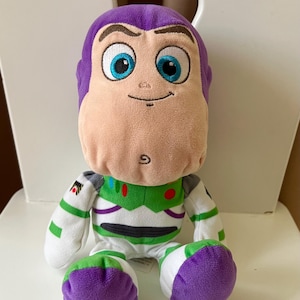Pode incluir: Um brinquedo de pel&uacute;cia de Buzz Lightyear, um personagem da franquia Toy Story. O brinquedo tem cabe&ccedil;a e p&eacute;s roxos, rosto bronzeado claro e um traje espacial verde e branco. O brinquedo est&aacute; sentado em uma cadeira branca.