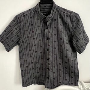 May include: Gray short-sleeved shirt with a mandarin collar and black buttons. The shirt features a vertical striped pattern with floral accents. The brand name "ATRIUM" is visible on the collar.