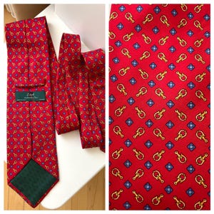 May include: Red silk tie with a repeating pattern of gold-colored key and lock motifs, interspersed with blue diamond shapes. The tie has a green lining and a label that reads "Zadi Andrew's Tie".