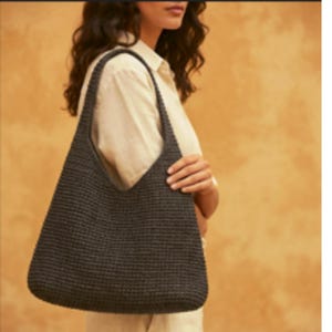 Op de afbeelding: Een donker antracietgrijze hobo-schoudertas met een dichte, uniforme gehaakte textuur. De tas heeft een brede, geïntegreerde schouderband die een doorlopend silhouet vormt met het hoofdgedeelte, wat zorgt voor een eenvoudig open ontwerp.